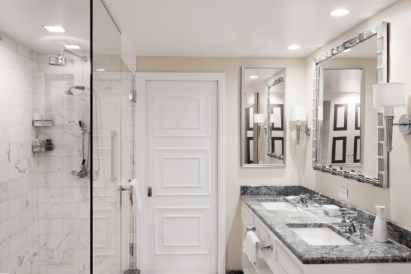 A modern bathroom with a glass shower, marble walls, and white door.