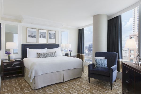 A well-appointed hotel room with a large bed, accent chair, and city view.