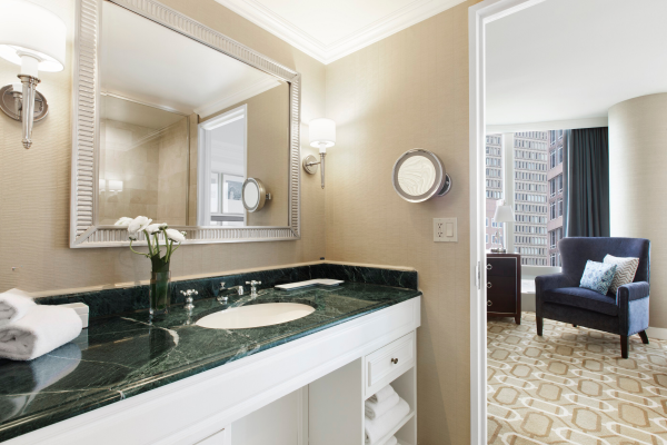 An elegant bathroom leading to a bedroom with a view of a cityscape.