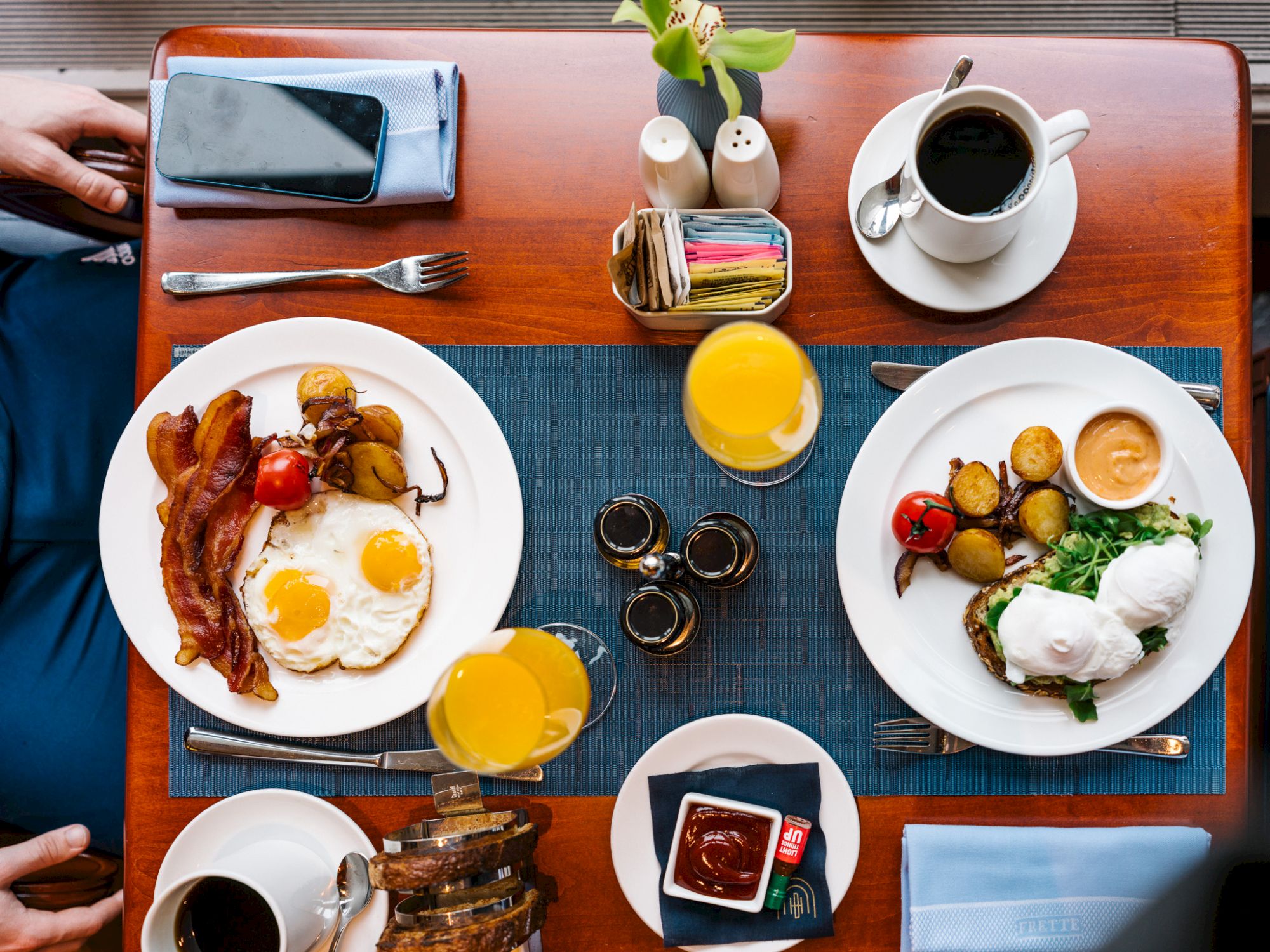 A breakfast spread with eggs, bacon, potatoes, toast, coffee, juice, and condiments neatly arranged on a table.