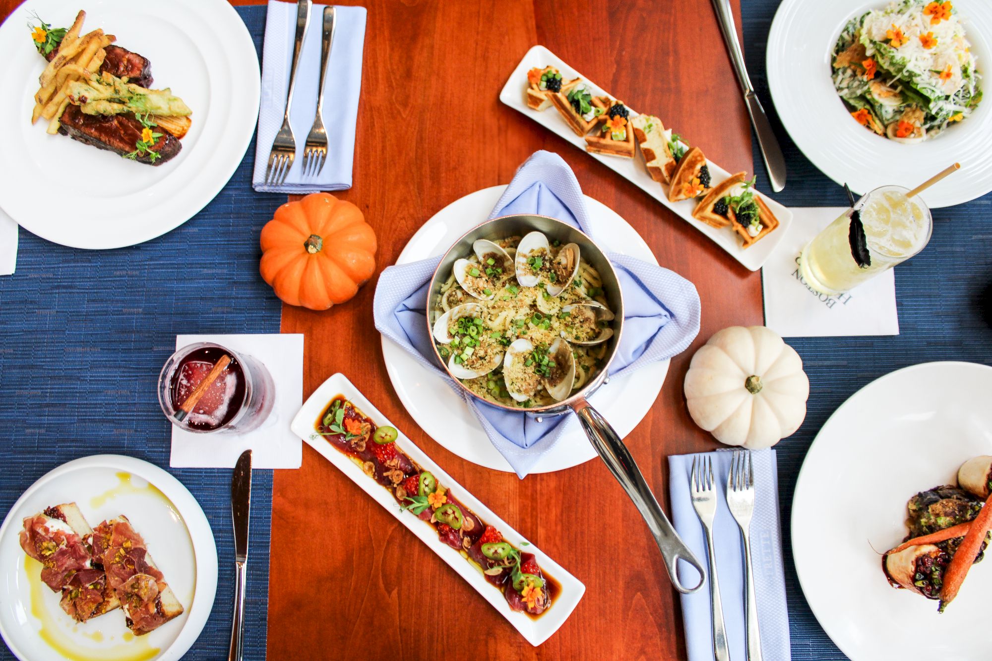 A table with pasta, bruschetta, salad, and drinks, decorated with pumpkins for an autumnal touch.