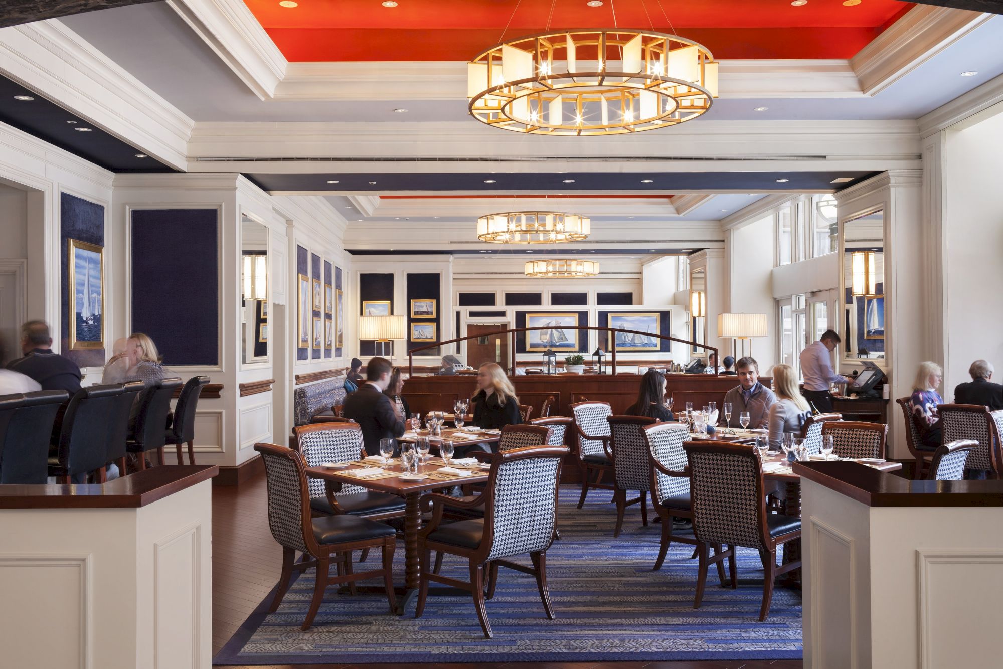 Elegant dining room with guests at tables and chandeliers overhead.