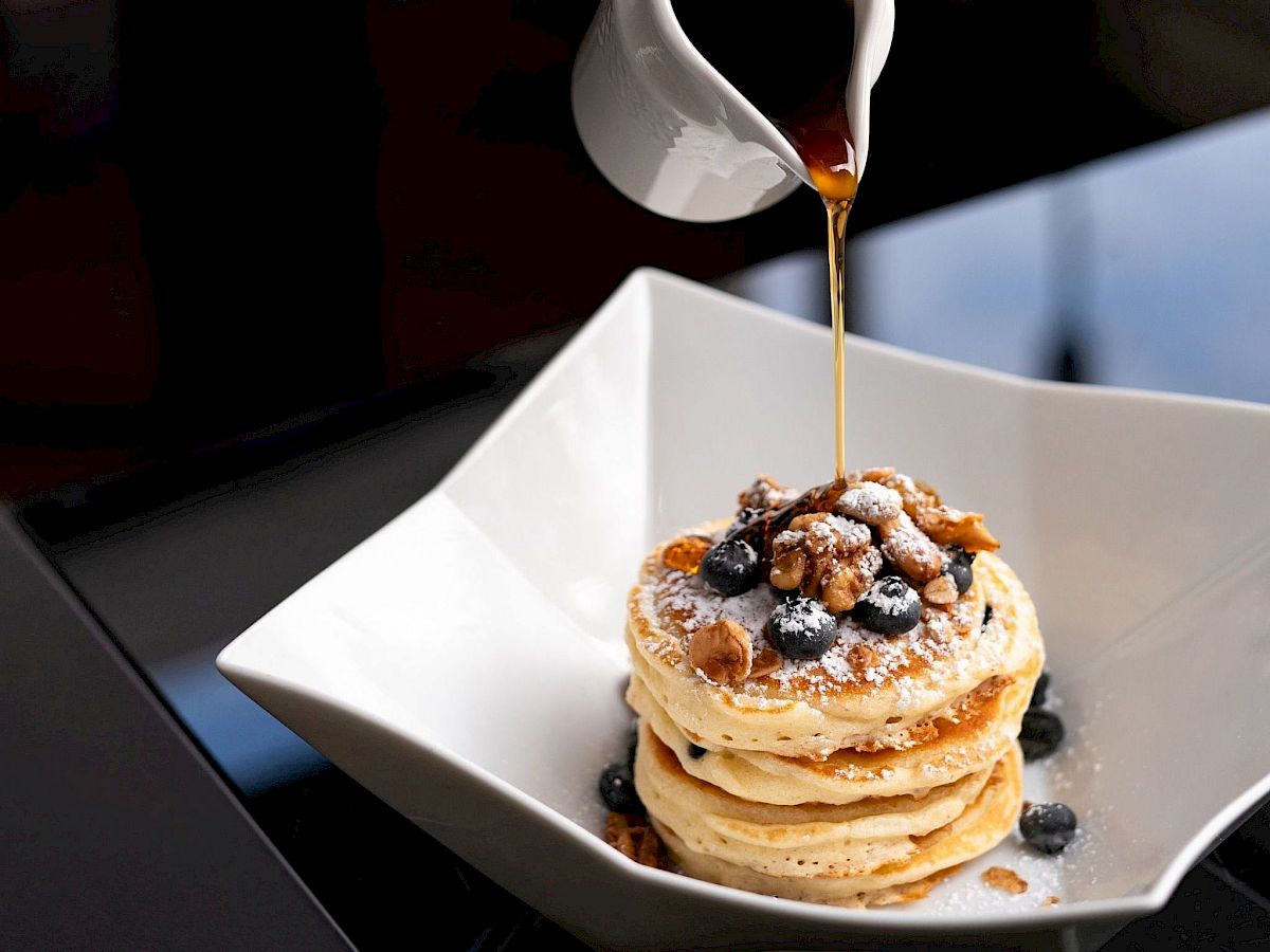 A person is pouring syrup on pancakes with berries.