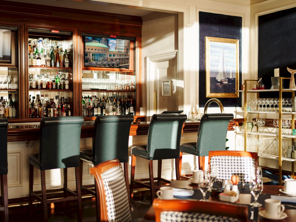 The image shows an elegant bar with stools, liquor shelves, and dining tables.