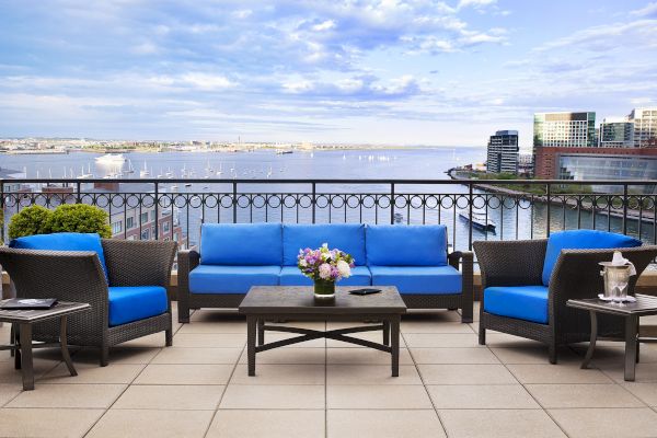 A balcony with blue sofas, table, and flowers overlooking a waterfront view.