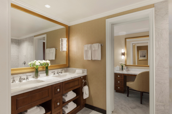 Elegant bathroom with dual sinks, mirrors, fresh flowers, and seating area.