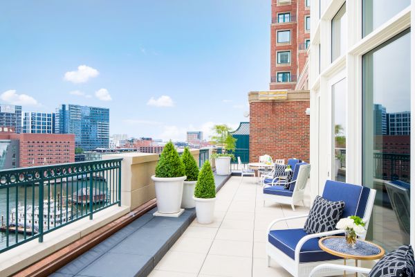 A sunny balcony with seating, plants, and a city view.