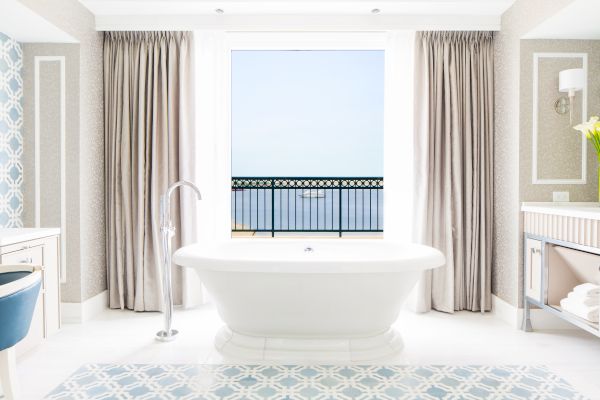 Bright bathroom with a freestanding tub, window view, and patterned floor.