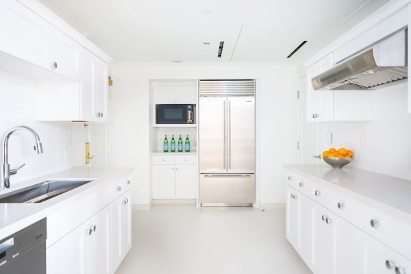 Modern white kitchen with appliances, cabinets, and fruit on the counter.