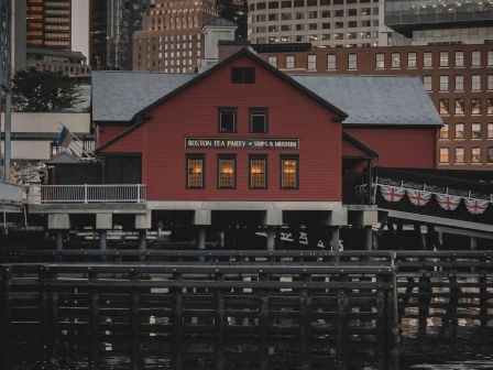 A red building by the water with city skyscrapers in the background.