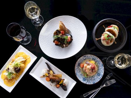 A top-down view of an elegant dining setup with various gourmet dishes and glasses of wine on a dark background.