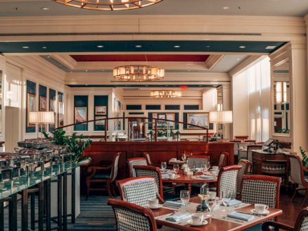 An elegant dining room with tables set for service, ambient lighting above.