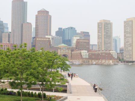 Cityscape with skyscrapers, a waterfront walkway, trees, and people