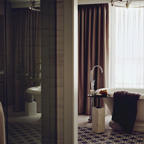 A luxurious bathroom with a freestanding bathtub, a floor lamp, a towel, and floor-to-ceiling curtains next to a large window.