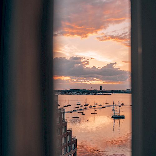 A picturesque sunset view through a window, showing a calm harbor with boats and a partly cloudy sky reflecting on the water.