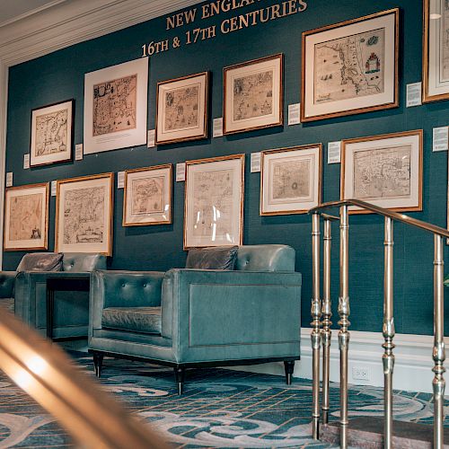 A room with framed artworks on the wall labeled "New England 18th & 19th Centuries," blue couches, and a railing in the foreground.