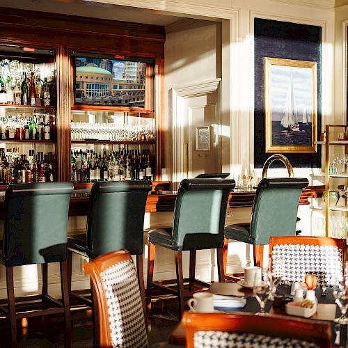 The image shows a bar area with high stools, a well-stocked liquor shelf, and a nearby dining setup with chairs and tables ready for service.