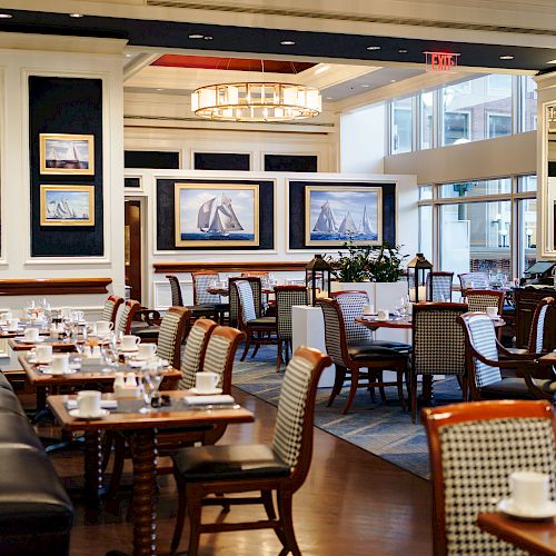 The image shows an elegant restaurant dining area with neatly arranged tables and chairs, nautical-themed paintings, and soft lighting.