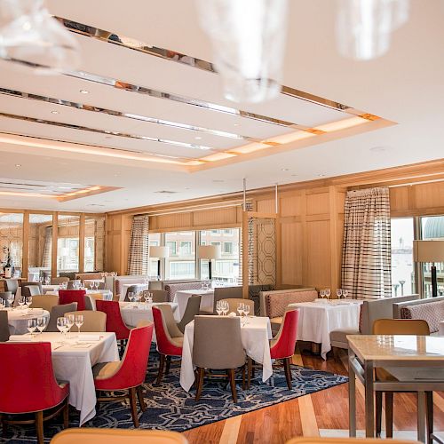 This image shows a well-decorated, elegant restaurant interior with neatly arranged tables and chairs, large windows, and warm lighting.