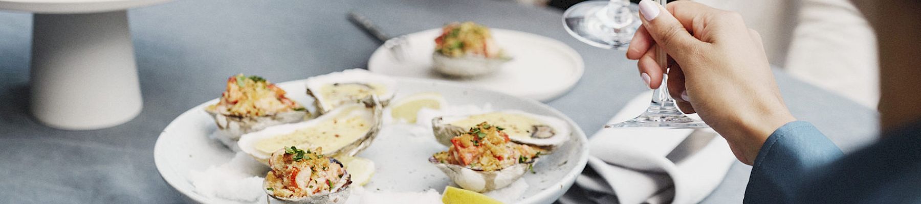 Two people are dining outdoors, clinking glasses with seafood dishes and cutlery on the table in front of them.