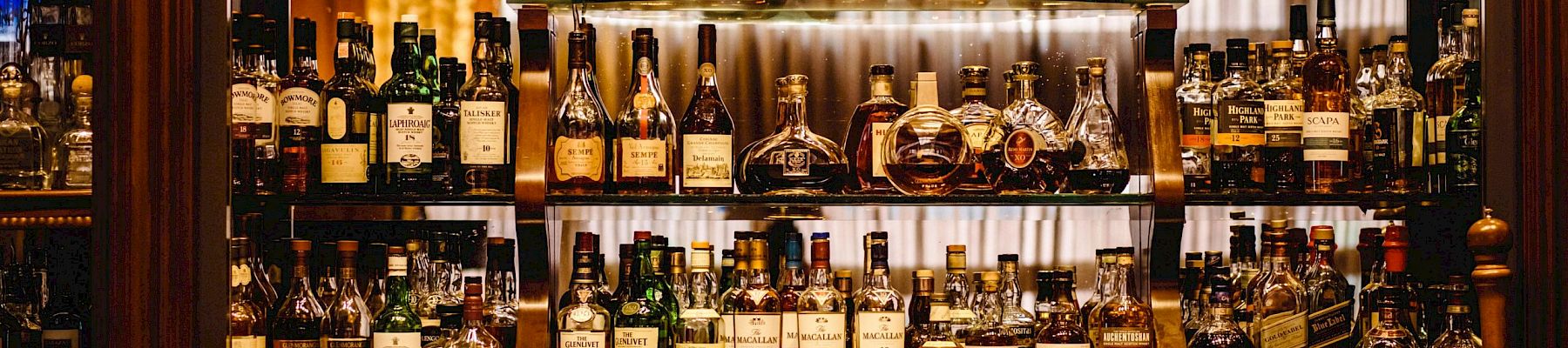 A well-stocked bar with various bottles of liquor including whiskey, rum, and other spirits arranged on shelves in a wooden setting.