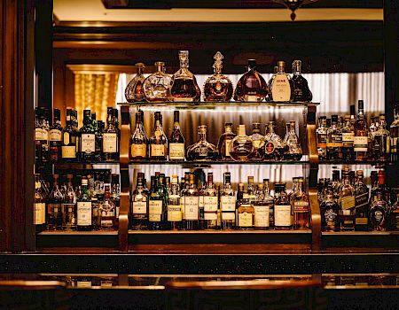 A well-stocked bar with various bottles of liquor including whiskey, rum, and other spirits arranged on shelves in a wooden setting.