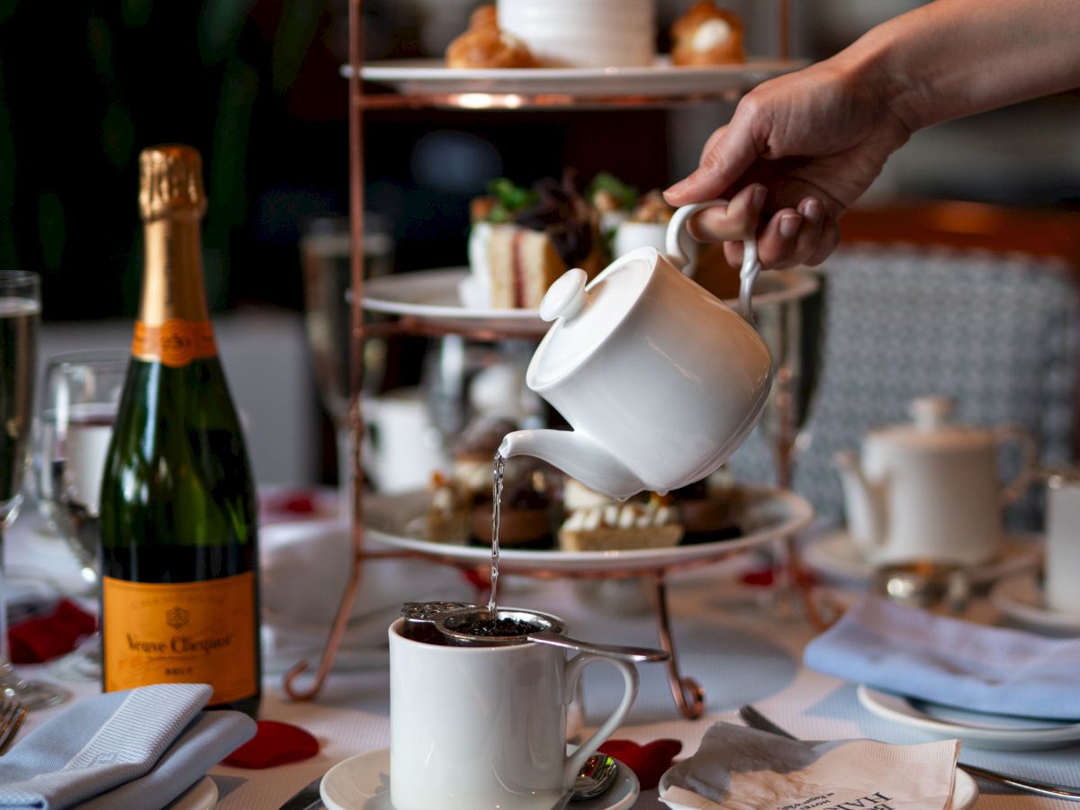 Elegant afternoon tea setup with a hand pouring tea, pastries on a tiered stand.