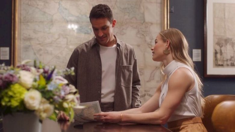 Two people are having a conversation over a book, with a map on the wall behind them.