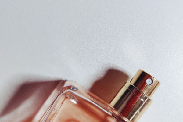 This image shows a close-up of a perfume bottle with a spray nozzle in focus. The bottle is partially filled with a light pink liquid.