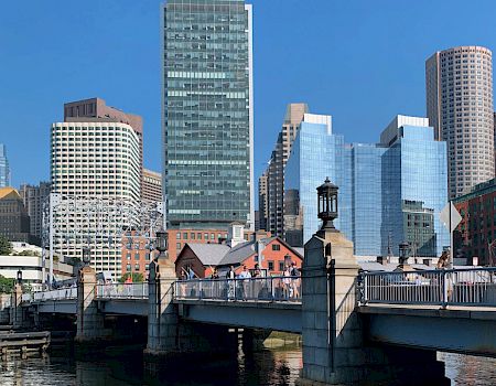 The image shows a cityscape with various skyscrapers, a bridge over water, and a clear blue sky in the background.