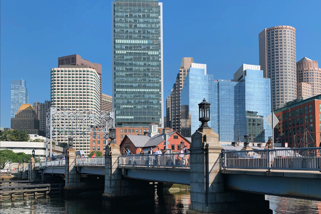 The image shows a cityscape with various skyscrapers, a bridge over water, and a clear blue sky in the background.