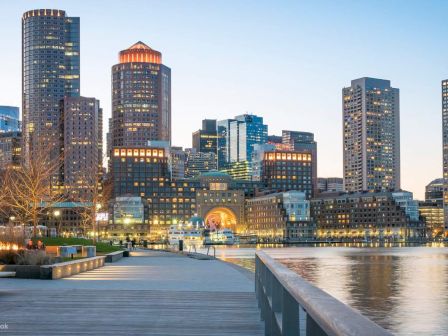 A waterfront and city skyline during twilight with lights reflecting on the water.