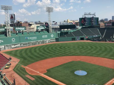 A baseball field with green grass, diamond infield, and stadium seats under a blue