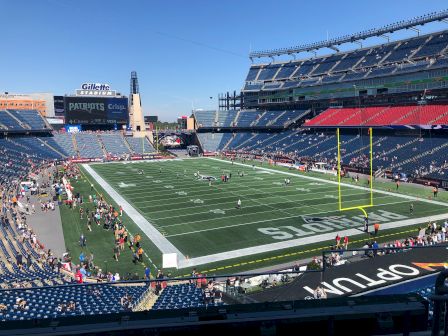 It's a sunny day at a football stadium with people on the field and in