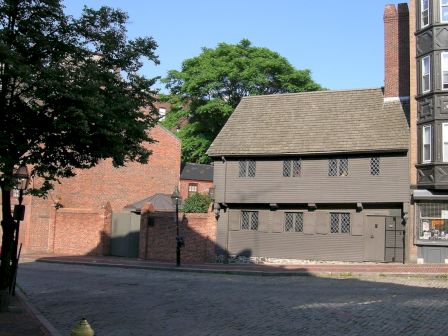 A cobblestone street with a historic wooden house, trees