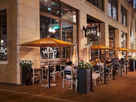 Image shows a street-side restaurant with outdoor seating and umbrellas at night.