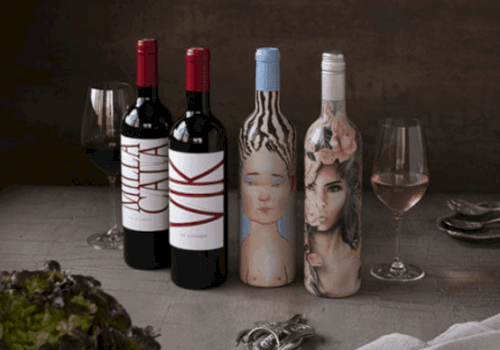 The image shows four wine bottles with artistic labels, two wine glasses, utensils, and lettuce on a table. Ends the sentence.