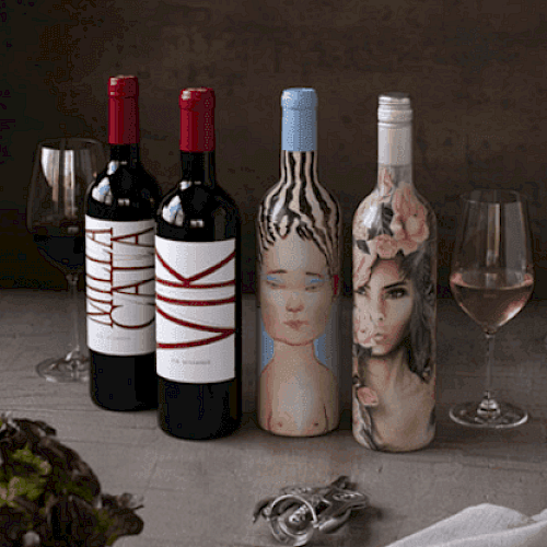 The image shows four wine bottles with artistic labels, two wine glasses, utensils, and lettuce on a table. Ends the sentence.