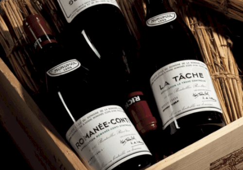 The image shows a wooden box containing several bottles of fine wine, including labels reading 