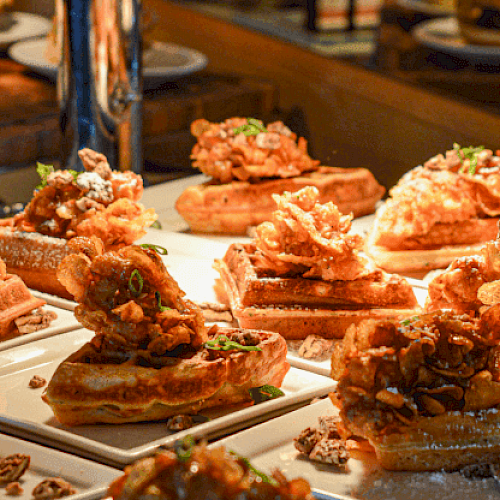 A buffet display of chicken and waffles garnished with herbs, arranged on plates under warm lighting, ready to be served.