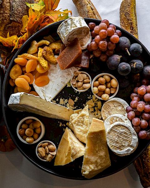 An assortment of cheeses, grapes, nuts, dried fruits, and bread are displayed on a platter alongside dishes of seafood and lemon wedges.