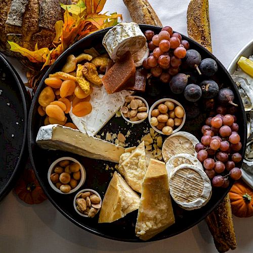 An assortment of cheeses, grapes, nuts, dried fruits, and bread are displayed on a platter alongside dishes of seafood and lemon wedges.