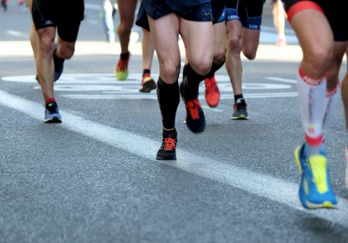 Runners in athletic wear and colorful shoes are participating in a race on a road marked with lines and a circular sign.