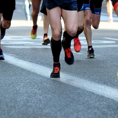 Runners in athletic wear and colorful shoes are participating in a race on a road marked with lines and a circular sign.