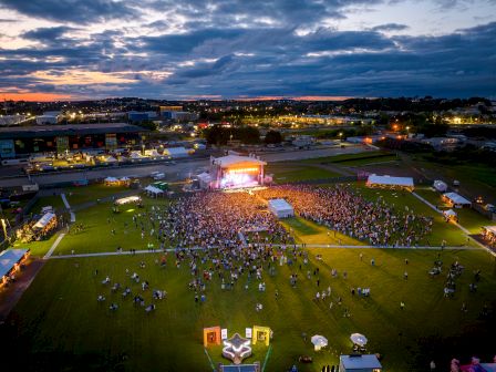 Outdoor event with a crowd facing a stage at dusk.
