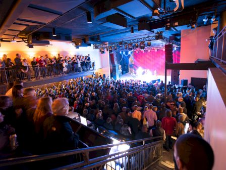 Audience watching a stage performance, with blue and purple stage lights.