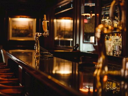 Dimly lit bar interior with stools, taps, and bottles.