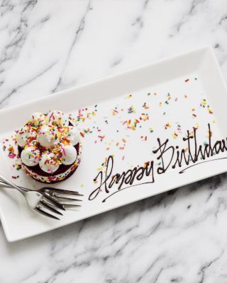 A birthday cupcake with sprinkles on a plate saying "Happy Birthday".