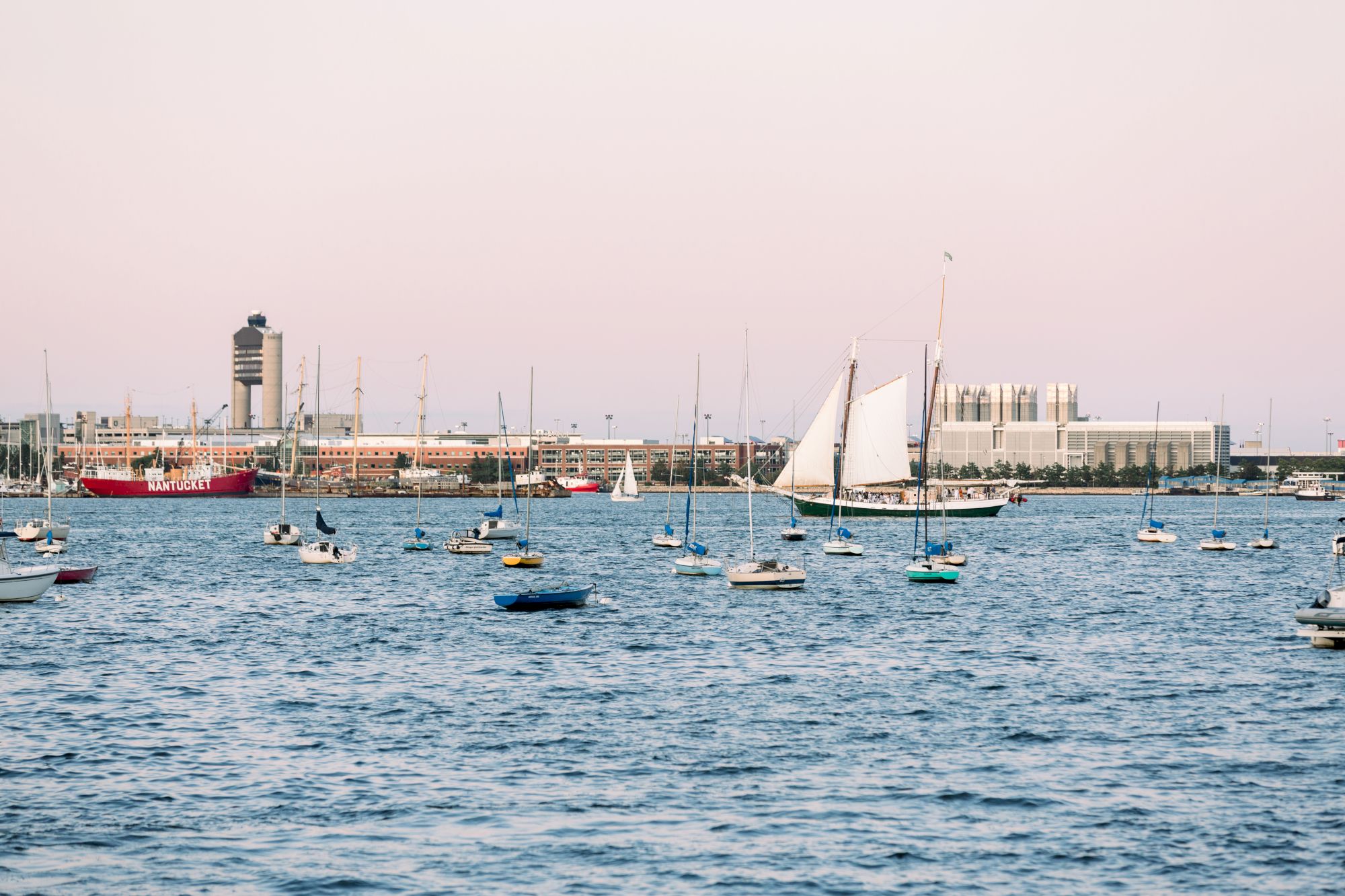 A harbor scene with boats, a sailboat in motion, and buildings in the distance.