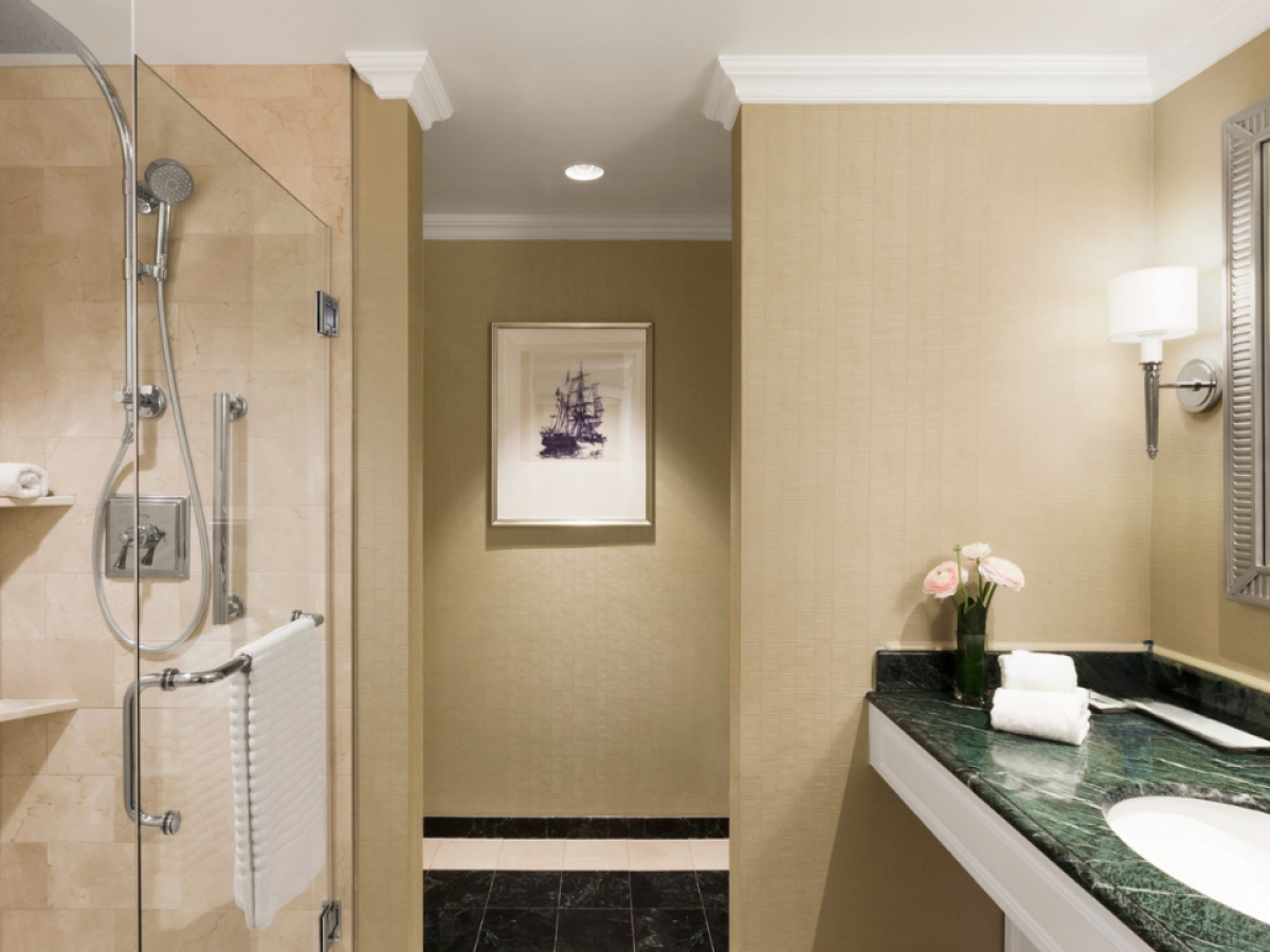 A modern bathroom with a glass shower, vanity sink, towels, and a framed